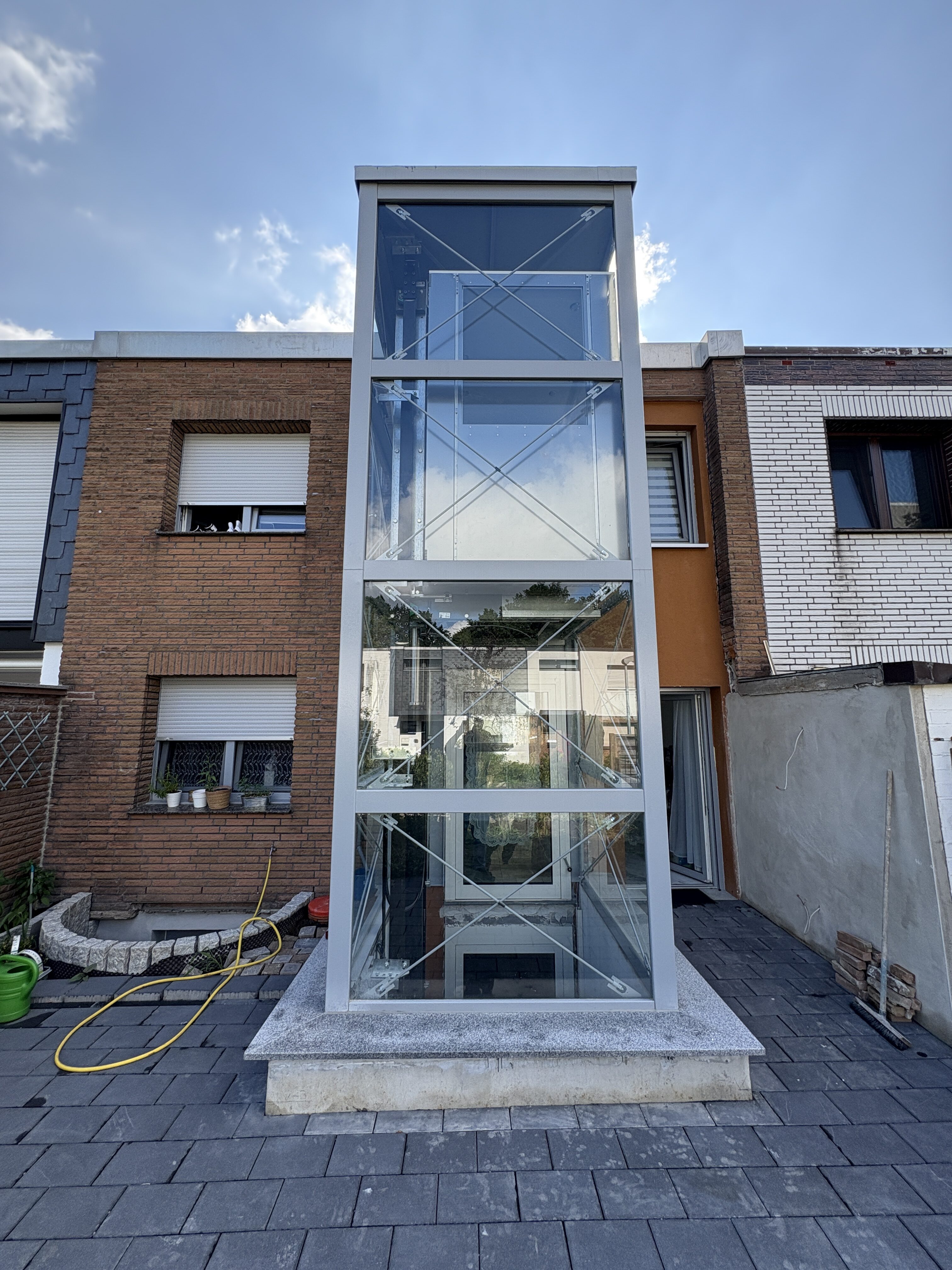 Außenaufzug an einem Backsteinhaus, mit gläserner Verkleidung und modernem Design.