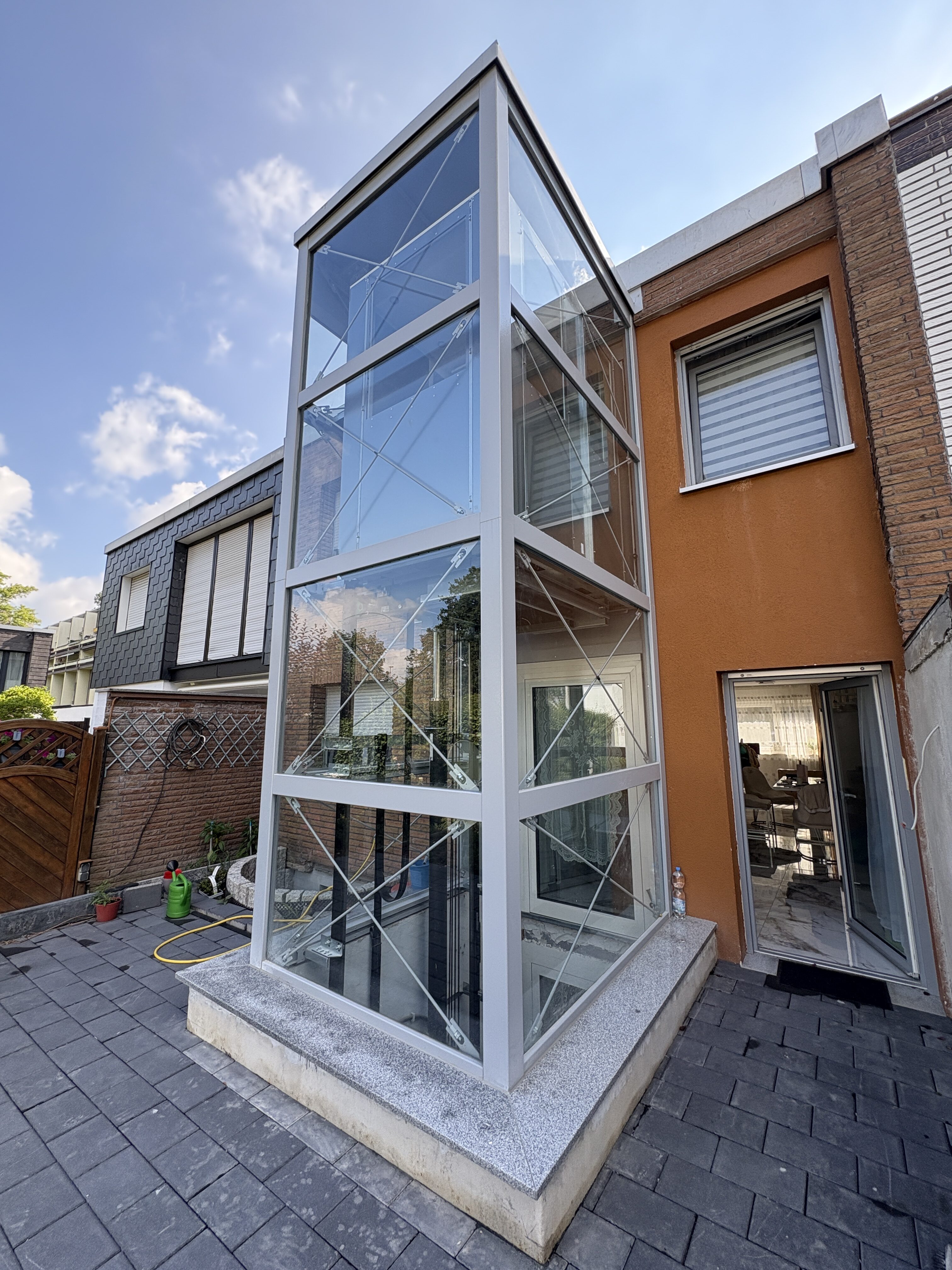 Außenaufzug an modernem Gebäude. Glas und Metall, reflektierender Himmel, sonnig, klare Linien.